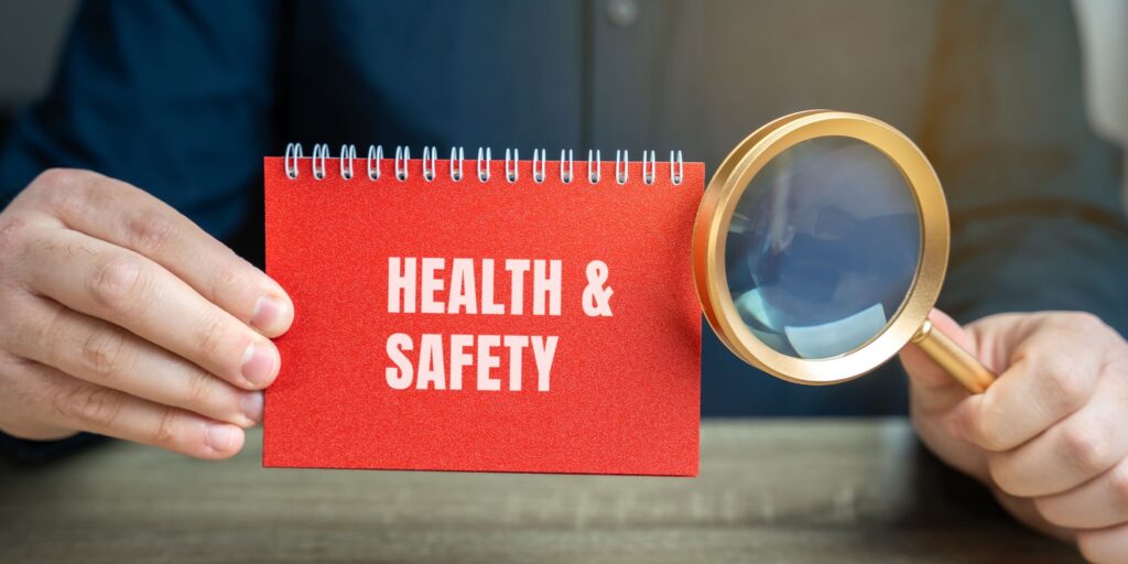 Close-up of a notepad reading health and safety beside a magnifying glass, representing the Health and Safety at Work Act 1974, and employer responsibilities for welfare, health, and safety.
